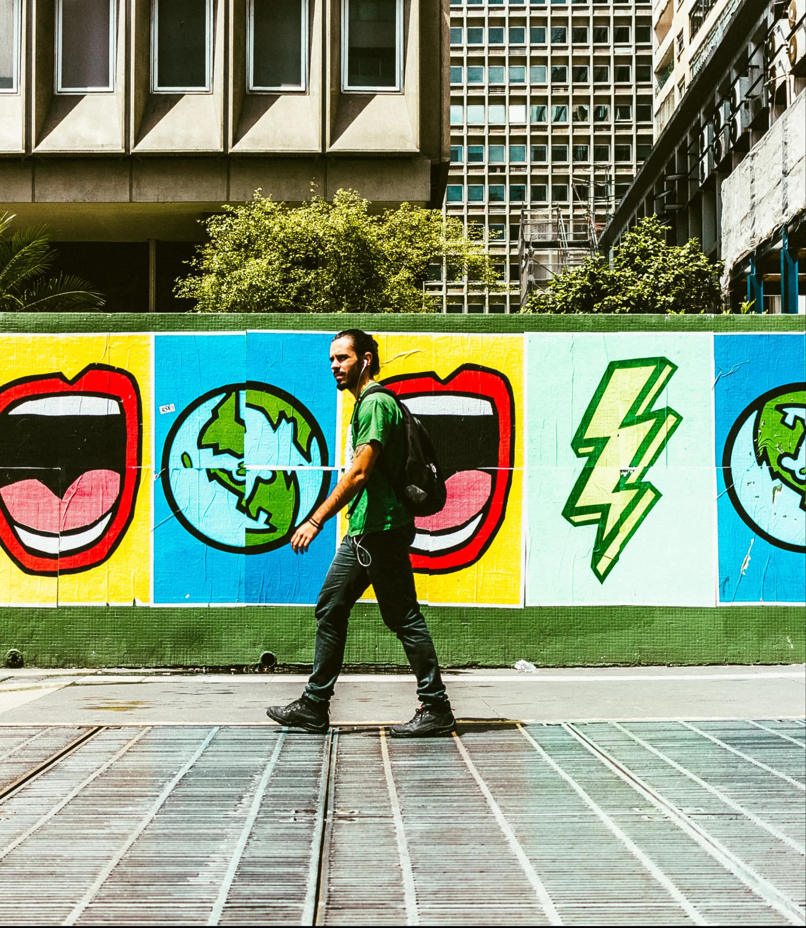 Homem caminhando na rua, com pôsteres coloridos ao fundo